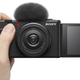 The Sony ZV-1F being held single-handedly with its preview screen folded out.
